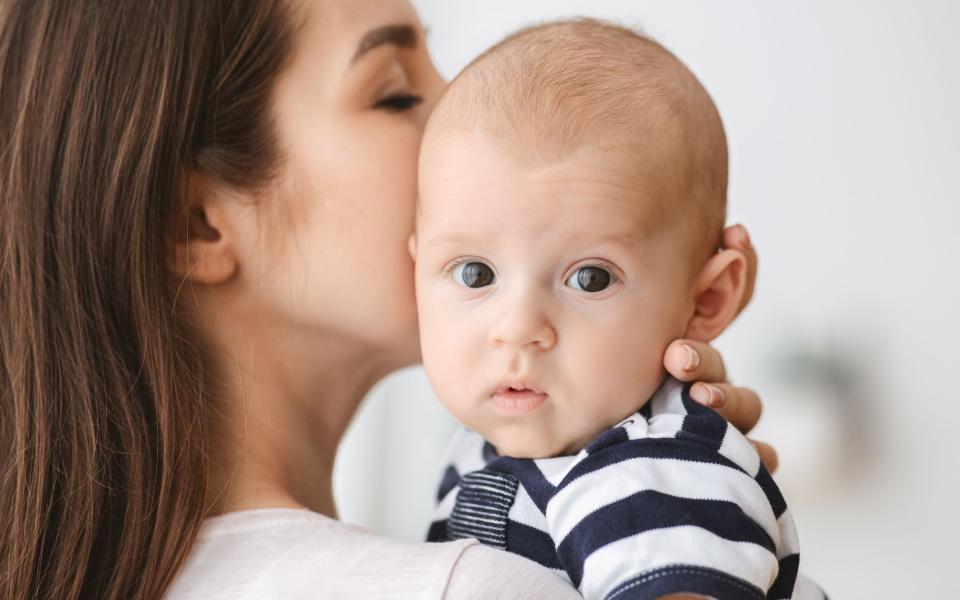 Moeder in close-up die haar baby een kus op de wang geeft. De baby kijkt naar de camera.