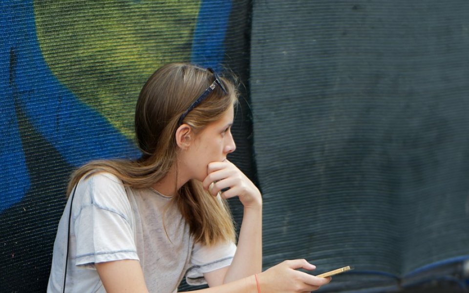 Tienermeisje zit op straat met smartphone op een zomerdag, nadenkend en starend in de verte