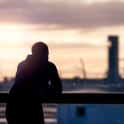 Man leunt op ballustrade en kijkt uit op stad bij zonsondergang