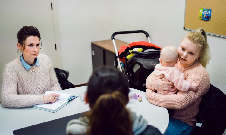 Verpleegkundige Dominique in overleg met een mama en medewerker van het OCMW