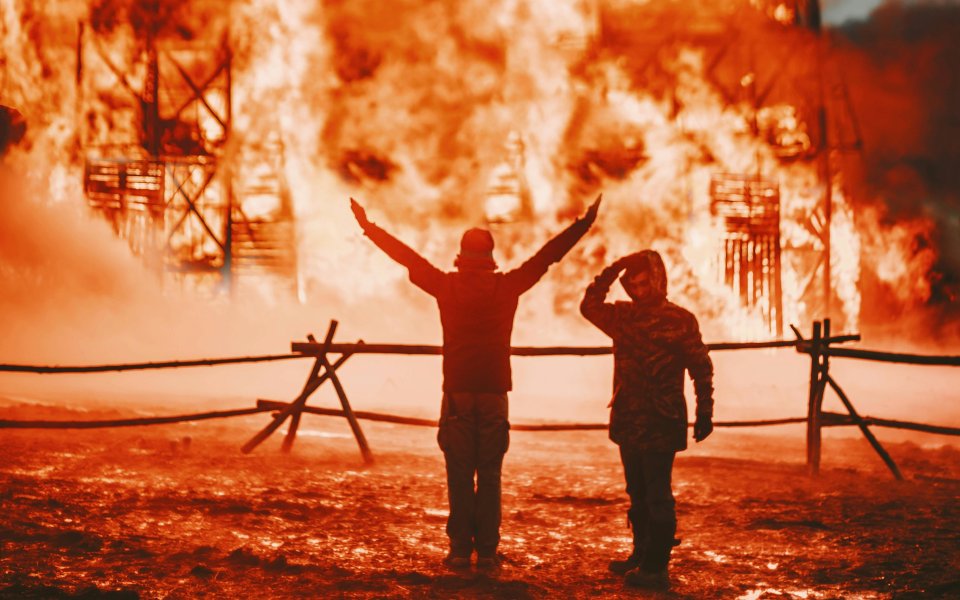 2-figuren-staan-te-kijken-naar-constructie-die-in-brand-staat