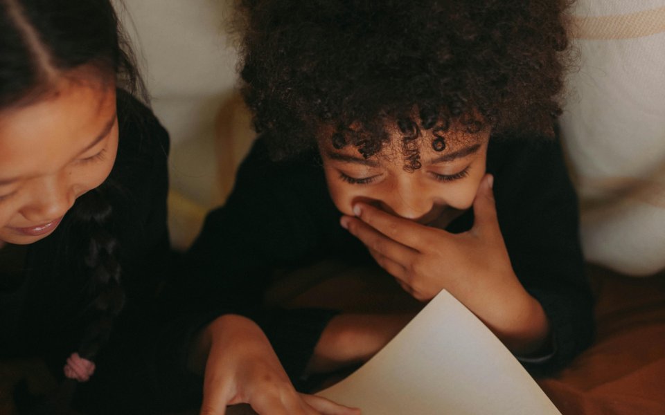 2 giechelende meisjes die lezen onder een deken