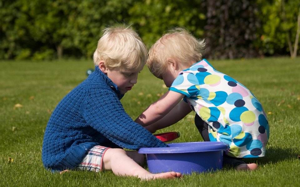 2 kleuters spelen samen buiten, zittend aan een kuipje