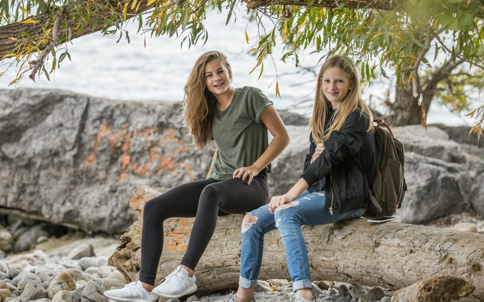 2-lachende-tienermeisjes--zittend-op-een-muurtje