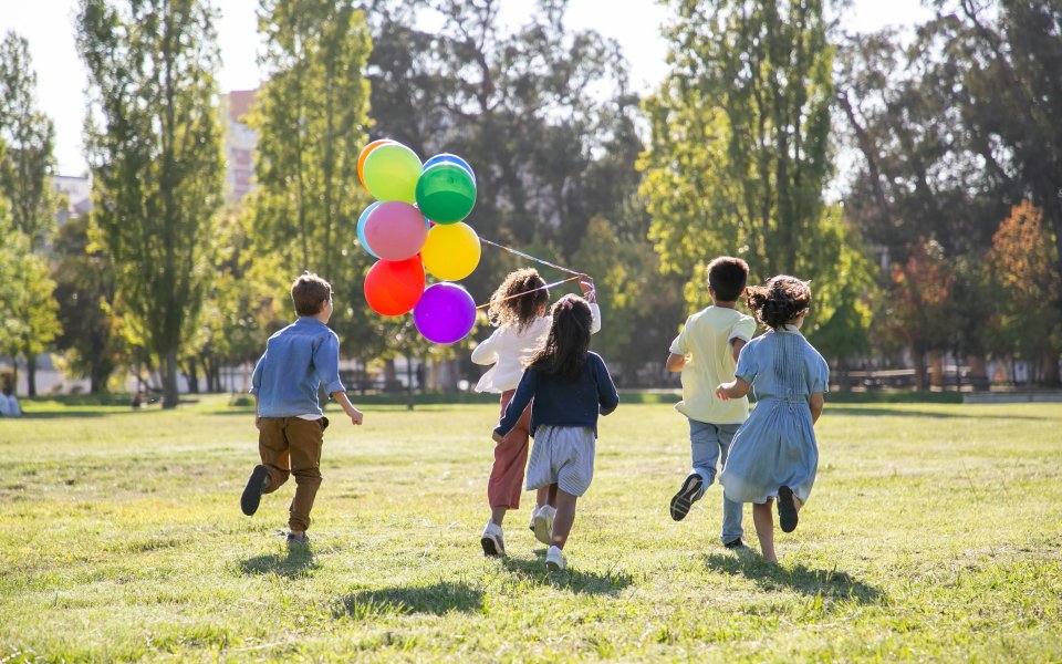 achteraanzicht groepje kinderen die lopen in een park met ballonnen
