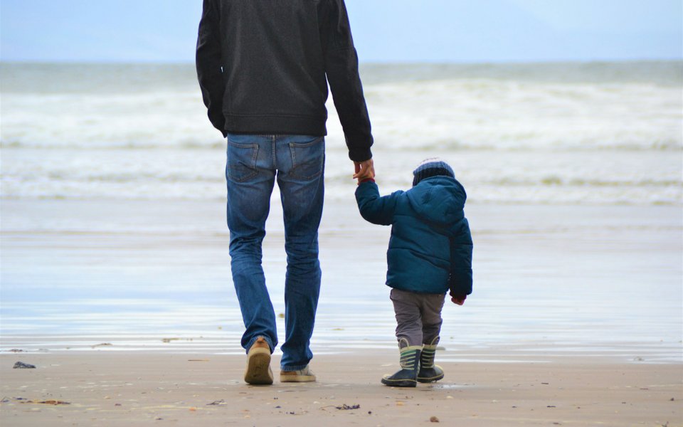 Nieuwsbericht Opgroeien Een man stapt met een kind op het strand richting de zee