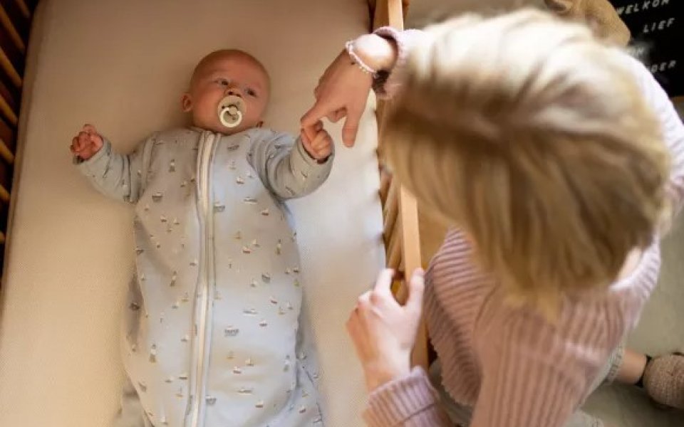Baby ligt in bedje met een slaapzak aan
