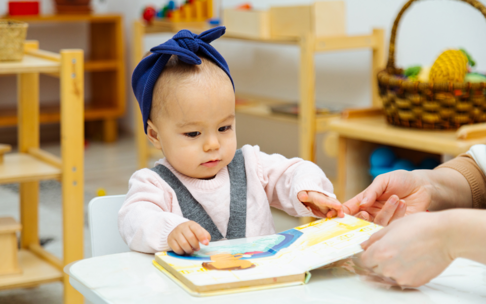 Baby kijkt naar prentenboek in bibliotheek met ouder of voorlezer, samen voorlezen met baby