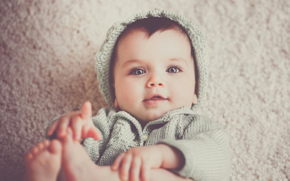 baby speelt met voetjes en kijkt in lens