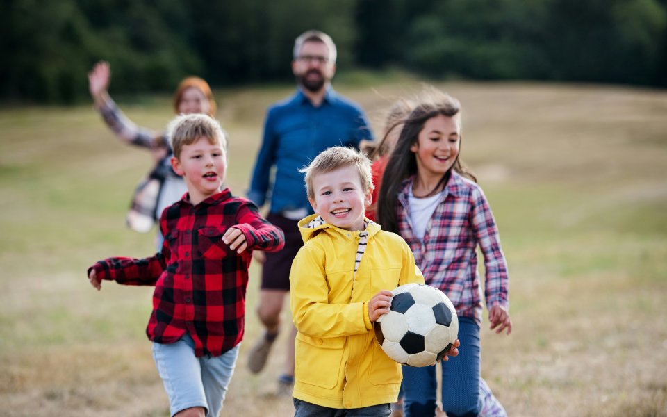 Kinderen spelen buiten met een voetbal, begeleiders op de achtergrond