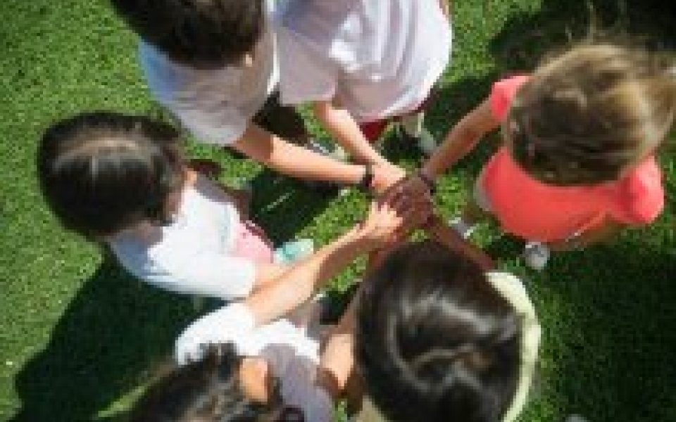 bovenaanzicht van 6 basisschool kinderen in een cirkel met hun handen naar het midden