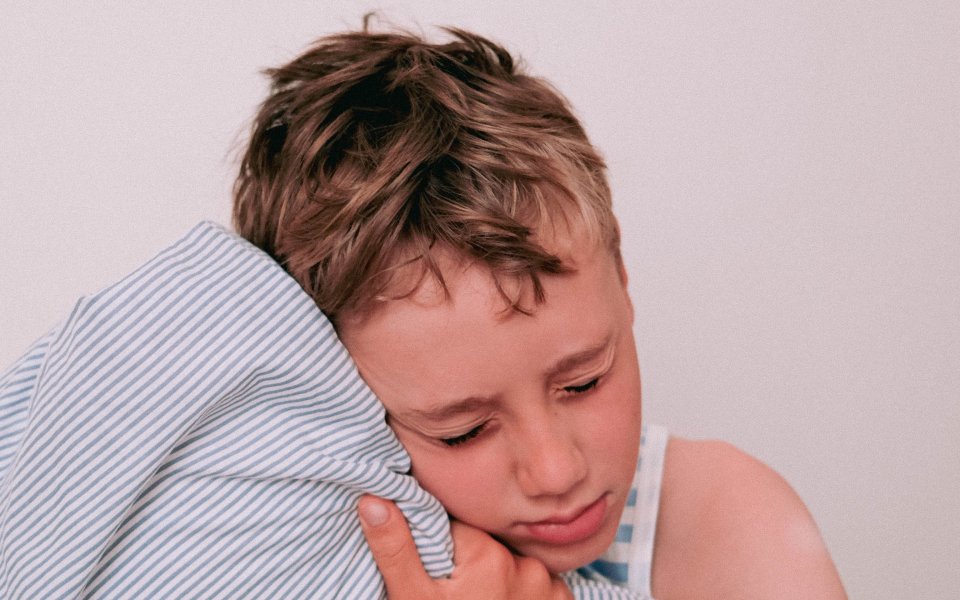 Een jonge jongen met een verdrietige uitdrukking omarmt een gestreept kussen, wat gevoelens van troost en melancholie oproept