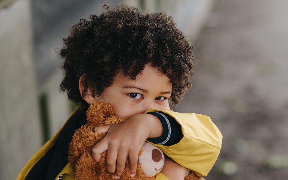 jongetje in een gele jas omarmt een teddybeer met een vage achtergrond