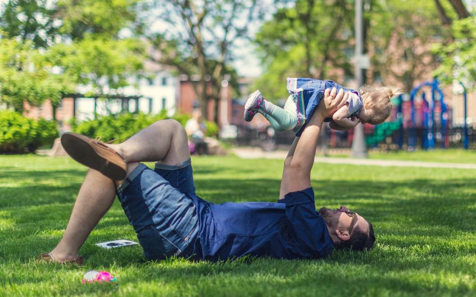 Papa ligt op gras en houdt kind boven zich