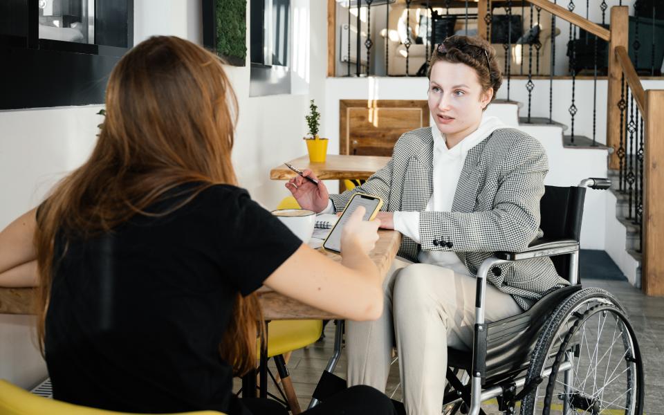 Vrouw in rolstoel praat met een andere vrouw aan een tafel