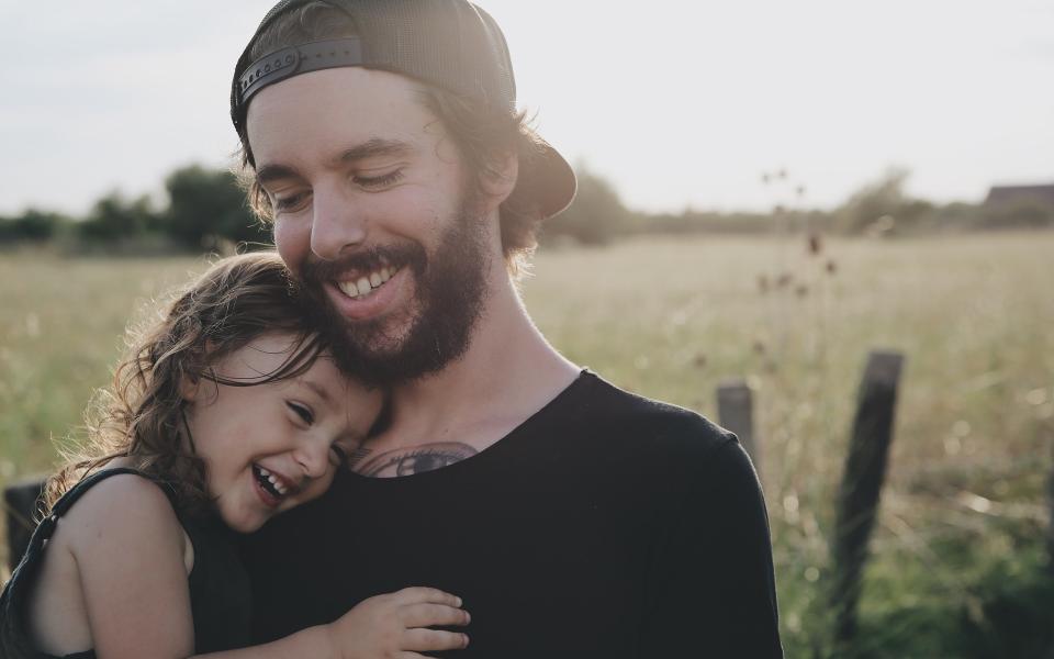 Lachende vader in een weide met een lachend kind op zijn arm