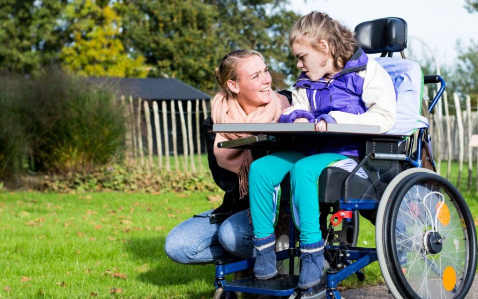 kind in rolstoel buiten met begeleider