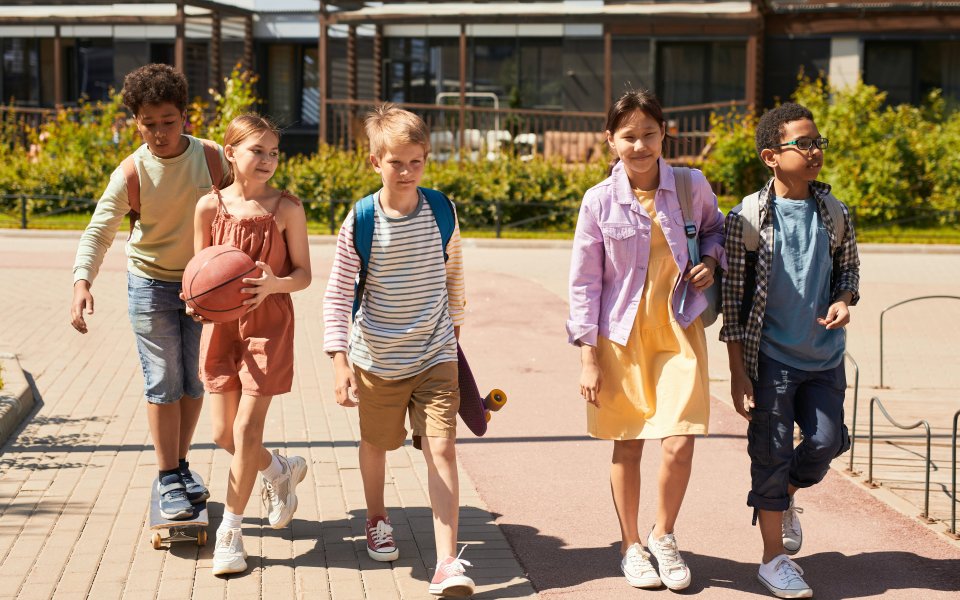 5 jonge tieners komen uit school met skateboard en basketbal