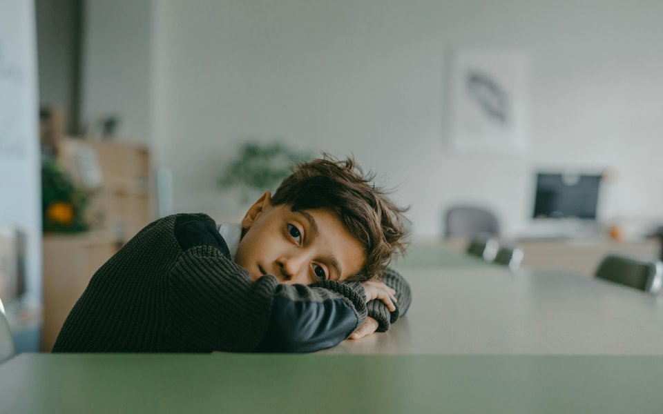jongen--met-hoofd-op-tafel--in-de-lens-kijkend