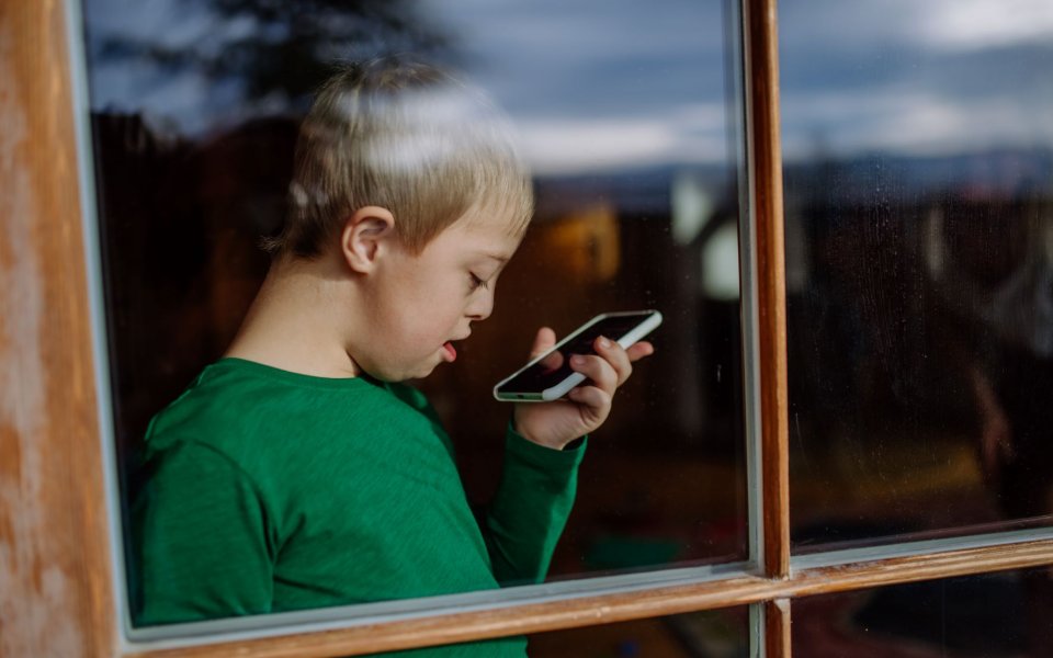 Jongen met downsyndroom, beperking, zorgbehoefte gebruikt zijn smartphone