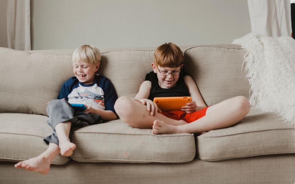 Jongens spelen spelletjes op hun eigen tablet en lachen in de zetel