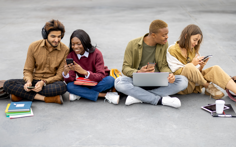 Vier jongeren zitten op plein met boeken, laptops, smartphones