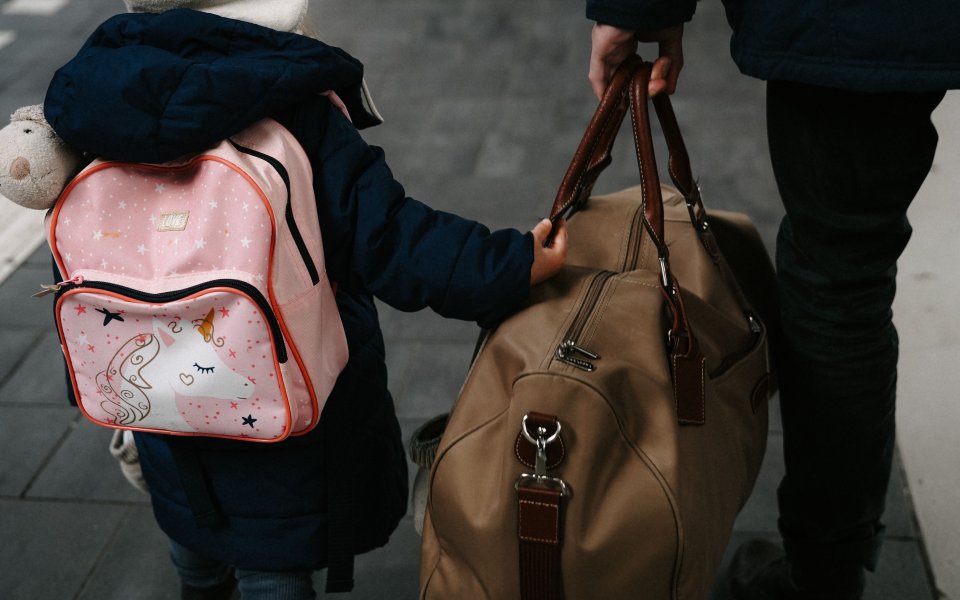 kind-op-rug-gezien-met-rugzakje-en-volwassene-die-grotere-tas-draagt
