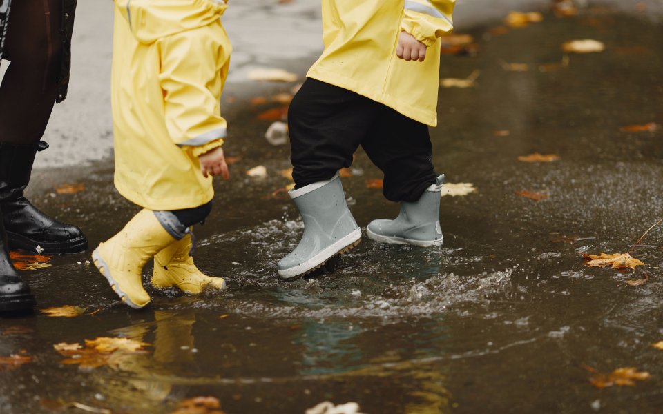 jonge kinderen spelen in de regen met regenjassen en regenlaarzen