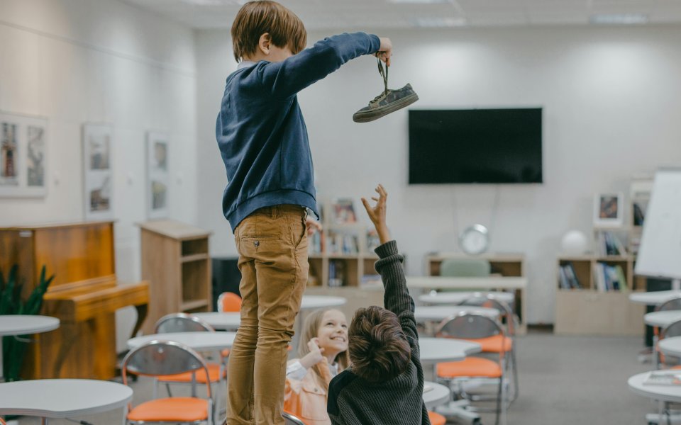 schooljongen staat op tafel en zwaait met afgepakte schoen, pesten in klaslokaal