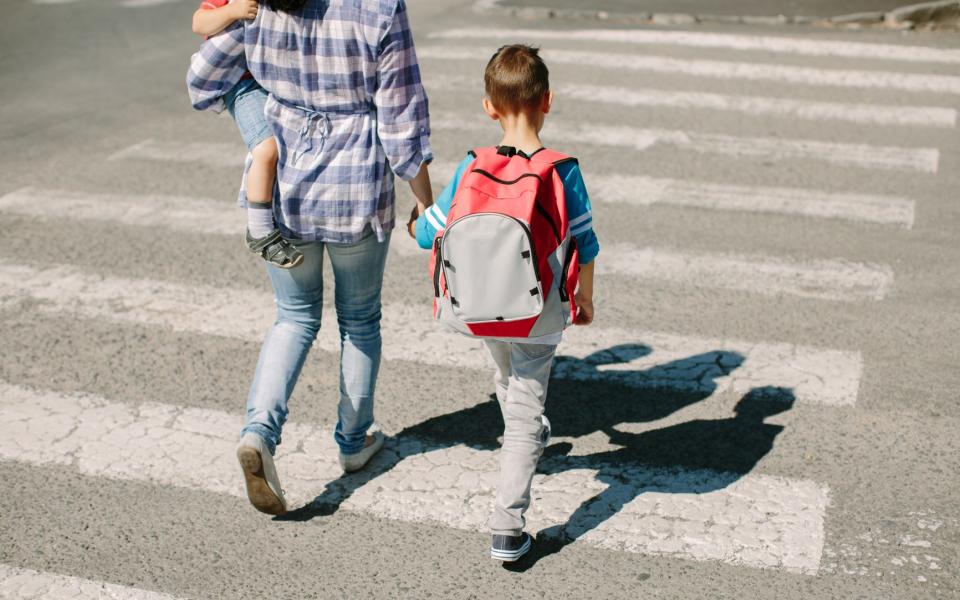 Mama steekt zebrapad over met kind op de arm en hand-in-hand met kind op weg naar school