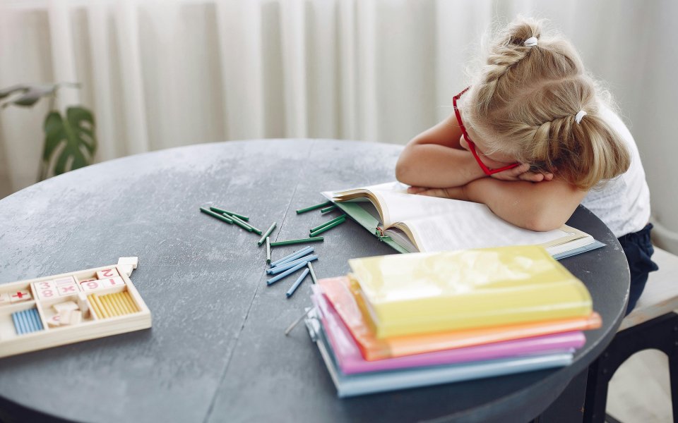 meisje aan tafeltje, ligt met hoofd op haar leerboek