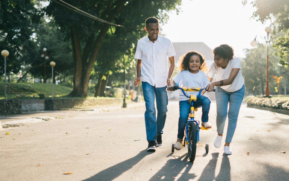 Meisje op fiets met hulp van mama en papa
