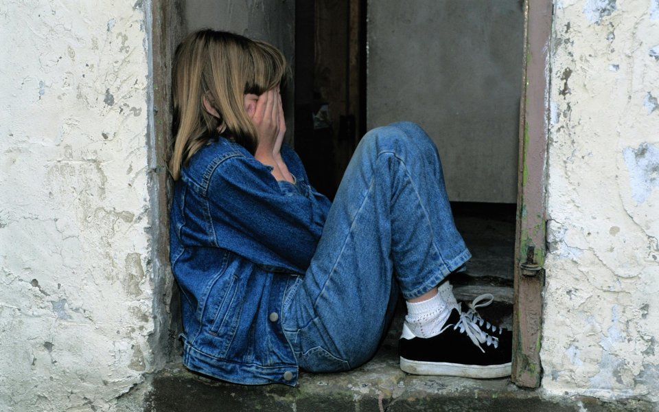 meisje-zit-in-deuropening-met-handen-voor-haar-gezicht