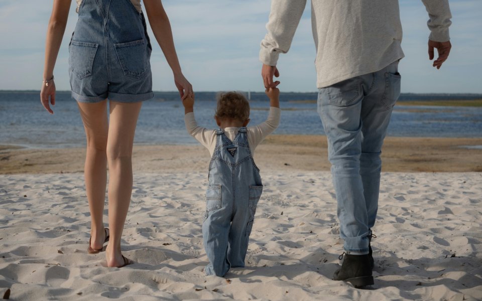 moeder-en-vader-met-stappende-baby-in-hun-midden--op-hun-achterzijde-gefotografeerd