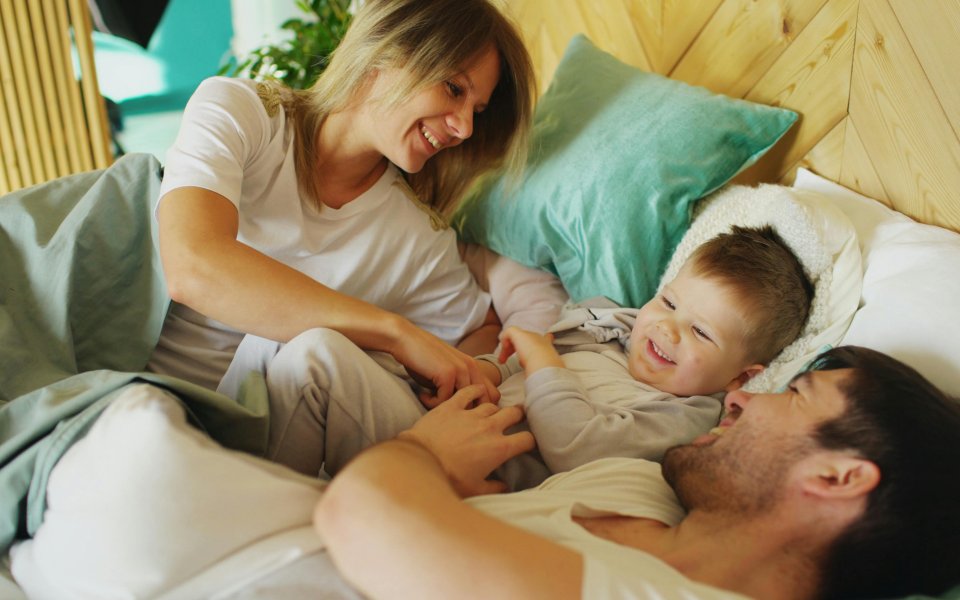 moeder-en-vader-spelend-in-bed-met-peuter