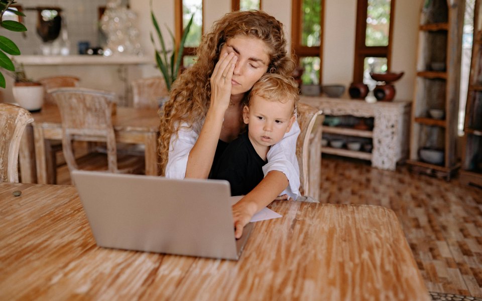 moeder-met-peuter-op-schoot-achter-laptop--vermoeid-in-ogen-wrijvend