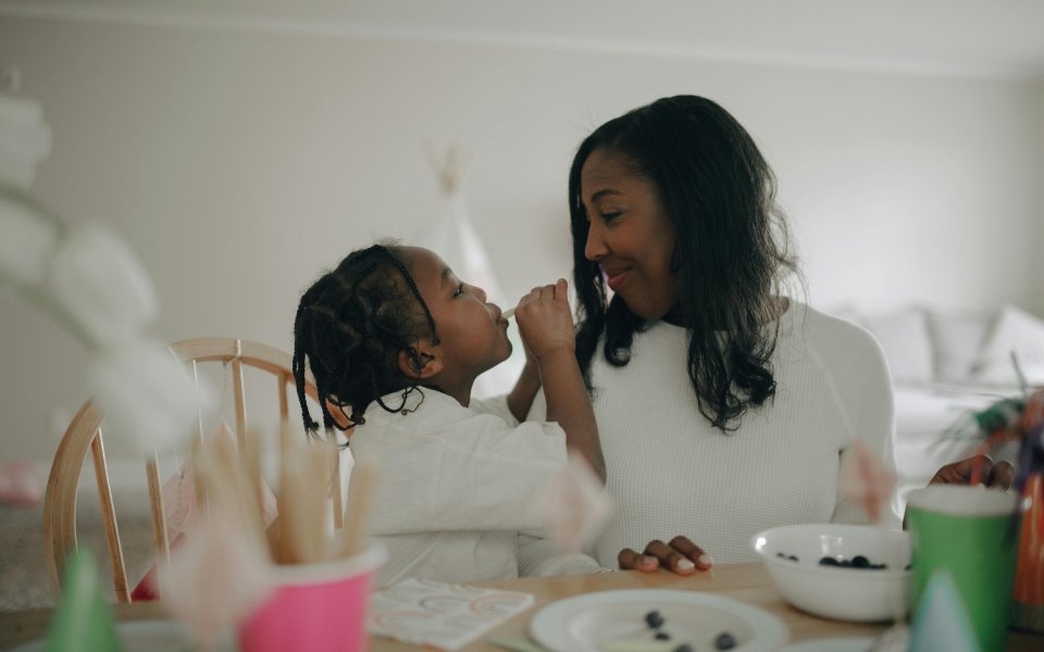 moeder-van-afrikaanse-origine-zit-glimlachend-met-dochter-aan-tafel