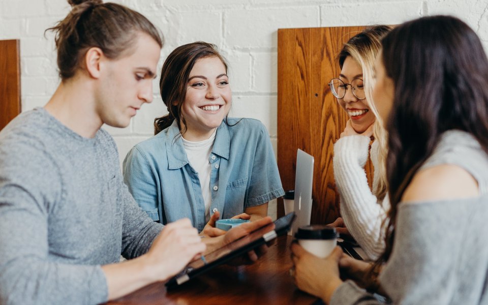 4 collega's staan bij elkaar rond een tafel tijdens een bespreking