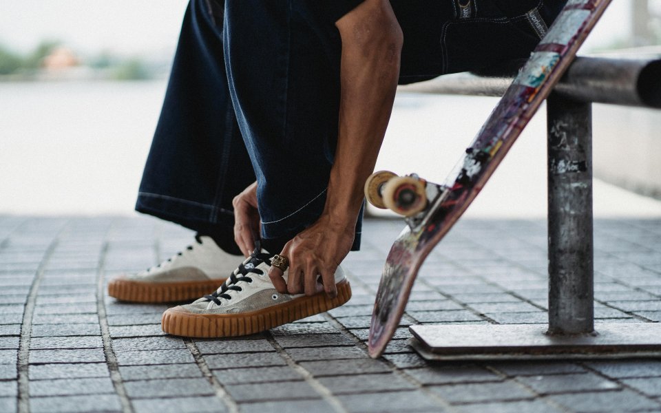 benen en voeten van jongere, gezeten op bank die schoen aandoet met naast zich een skateboard
