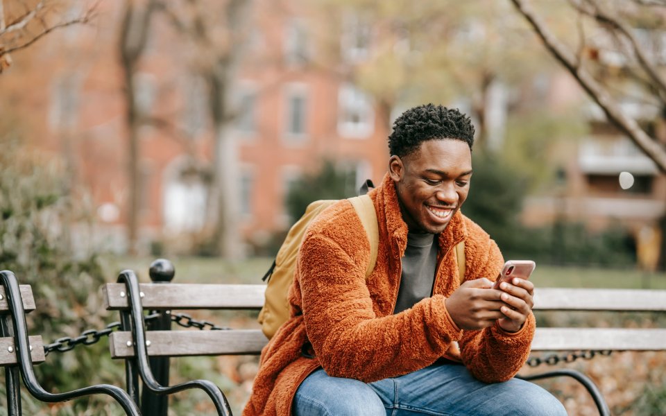 jongen, zittend op bank en lachend naar gsm kijkend