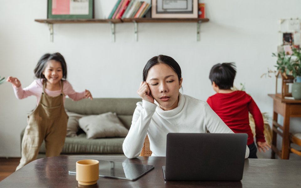 moeder achter laptop met spelende kinderen op achtergrond
