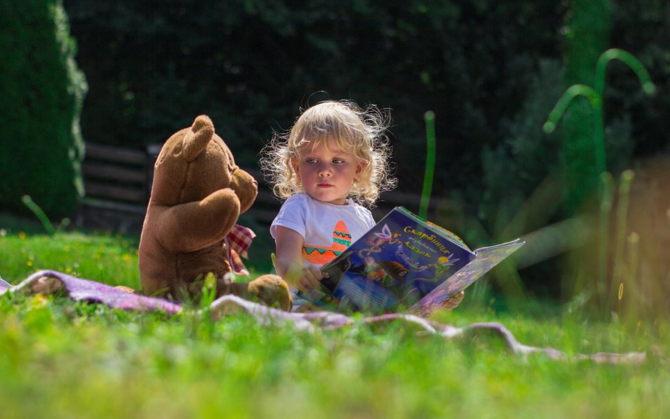 peuter zit in gras met boekje en grote knuffelbeer