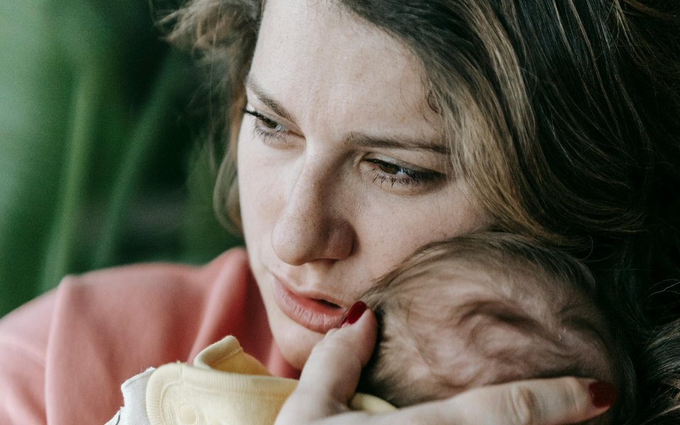 moeder kijkt ongelukkig, terwijl ze baby tegen zich aangedrukt houdt