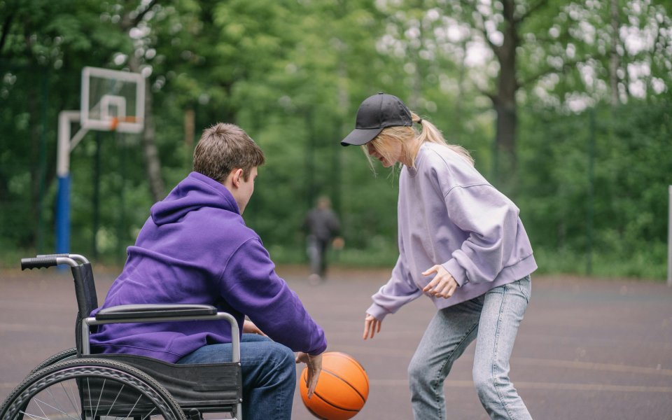 jongen in rolstoel en meisje spelen samen basket op een pleintje
