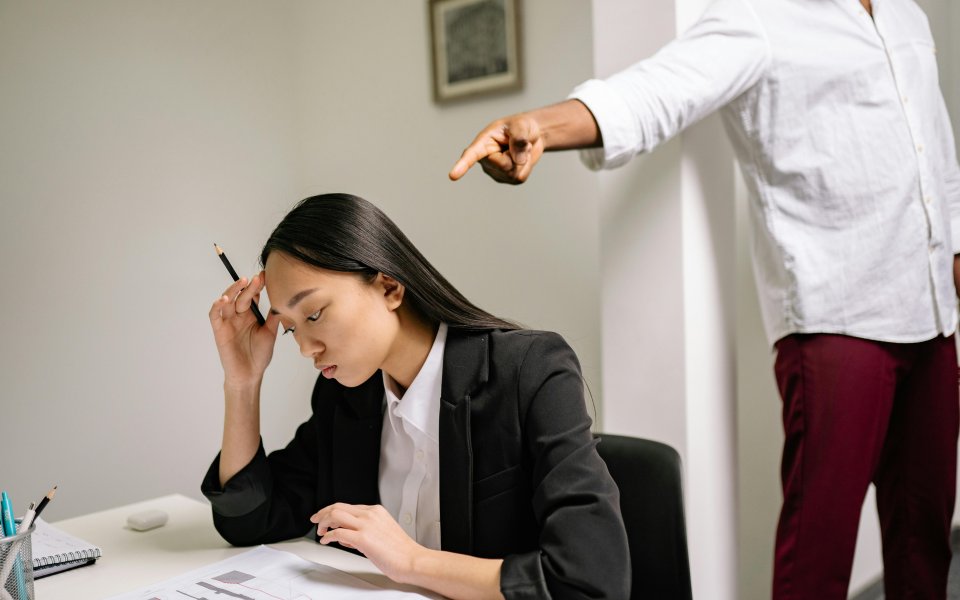 iemand wijst beschuldigend naar een vrouw aan haar bureau