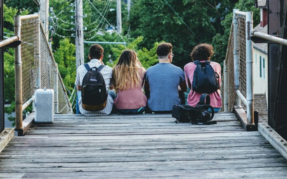 Nieuwsbericht Opgroeien Vier jongeren zitten met hun rug naar de camera op een hangbrug