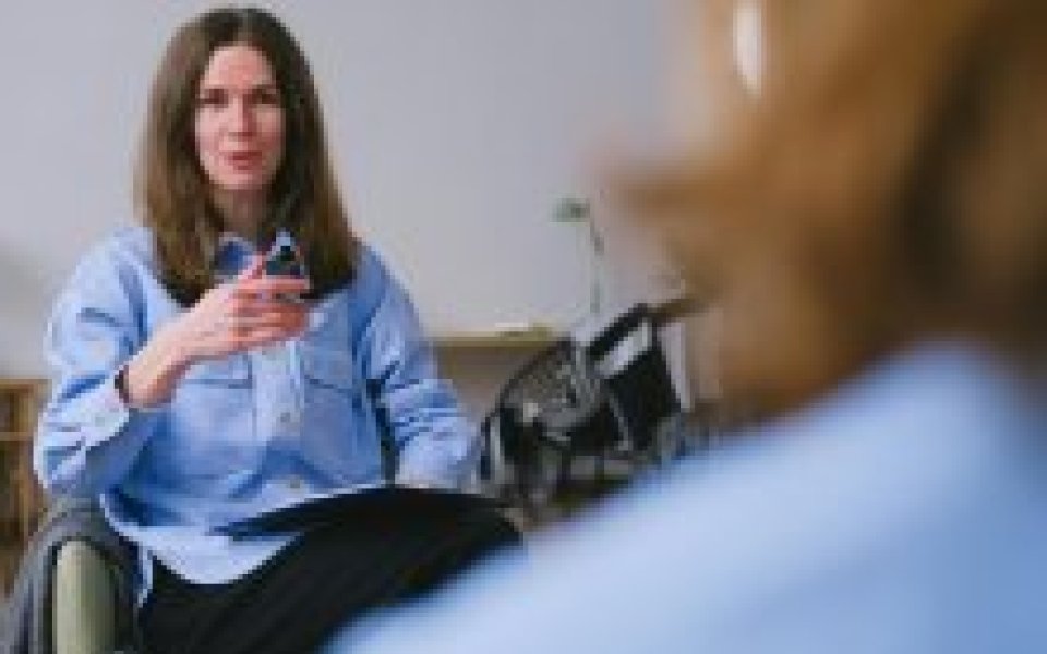 professional met schriftje op haar schoot kijkt naar een vrouw waarvan je de rug ziet