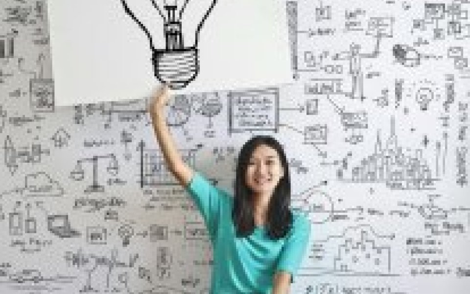 tiener zit in kleermakerszit en houdt een groot papier met een getekende gloeilamp omhoog