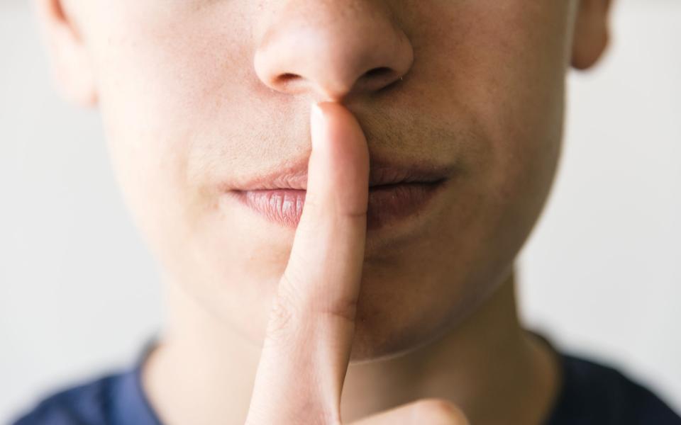 Tienerjongen met vinger op de lippen, teken voor stilzwijgen