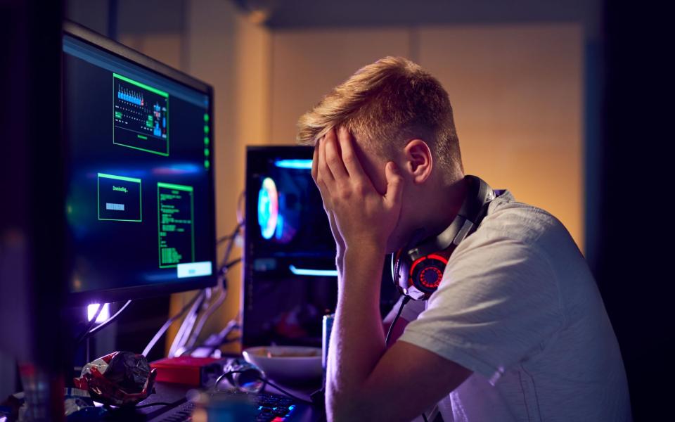 Tienerjongen met handen voor ogen zit aan computer, gepeste tiener tijdens gaming